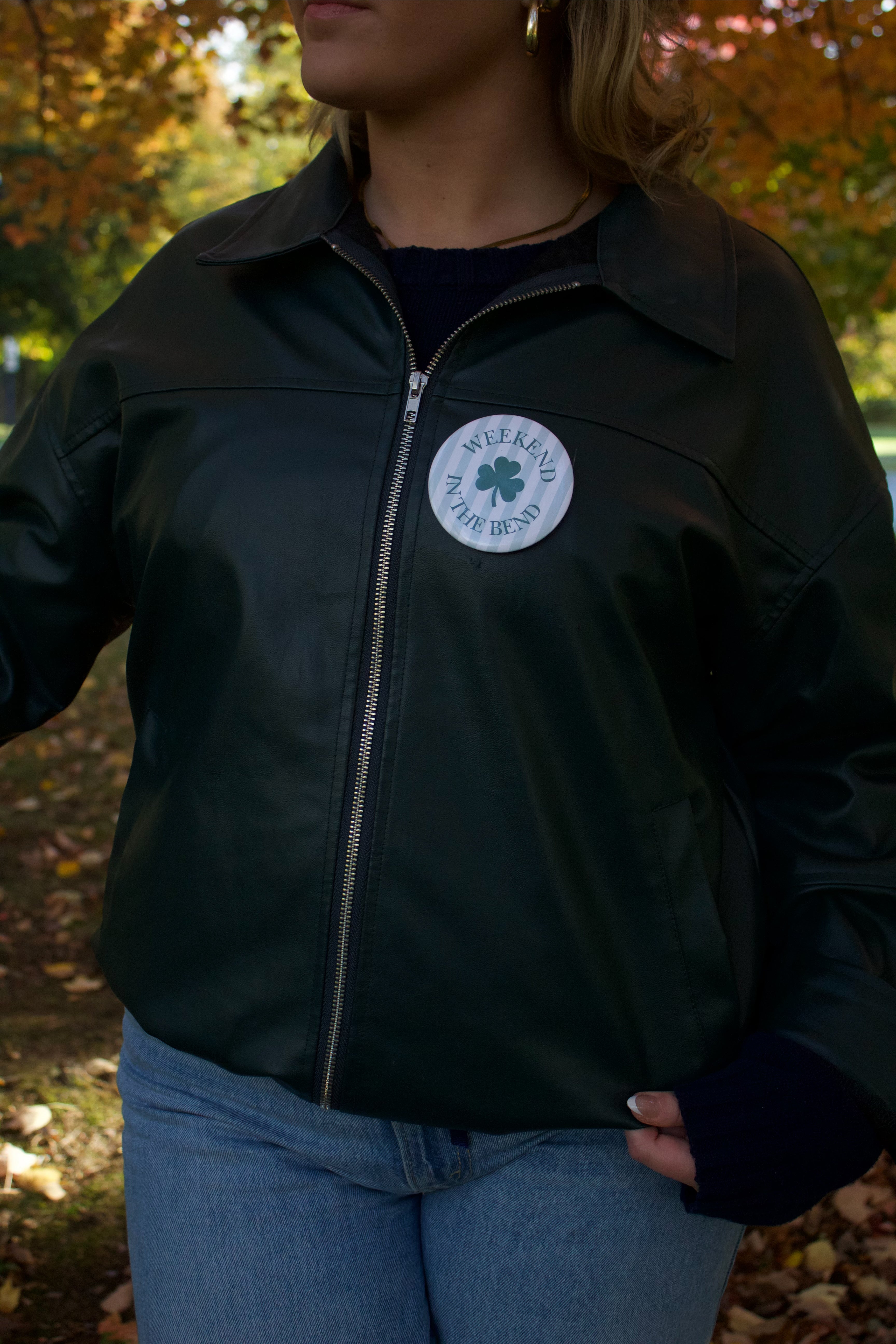 Person wearing a black leather jacket with a logo in an outdoor setting