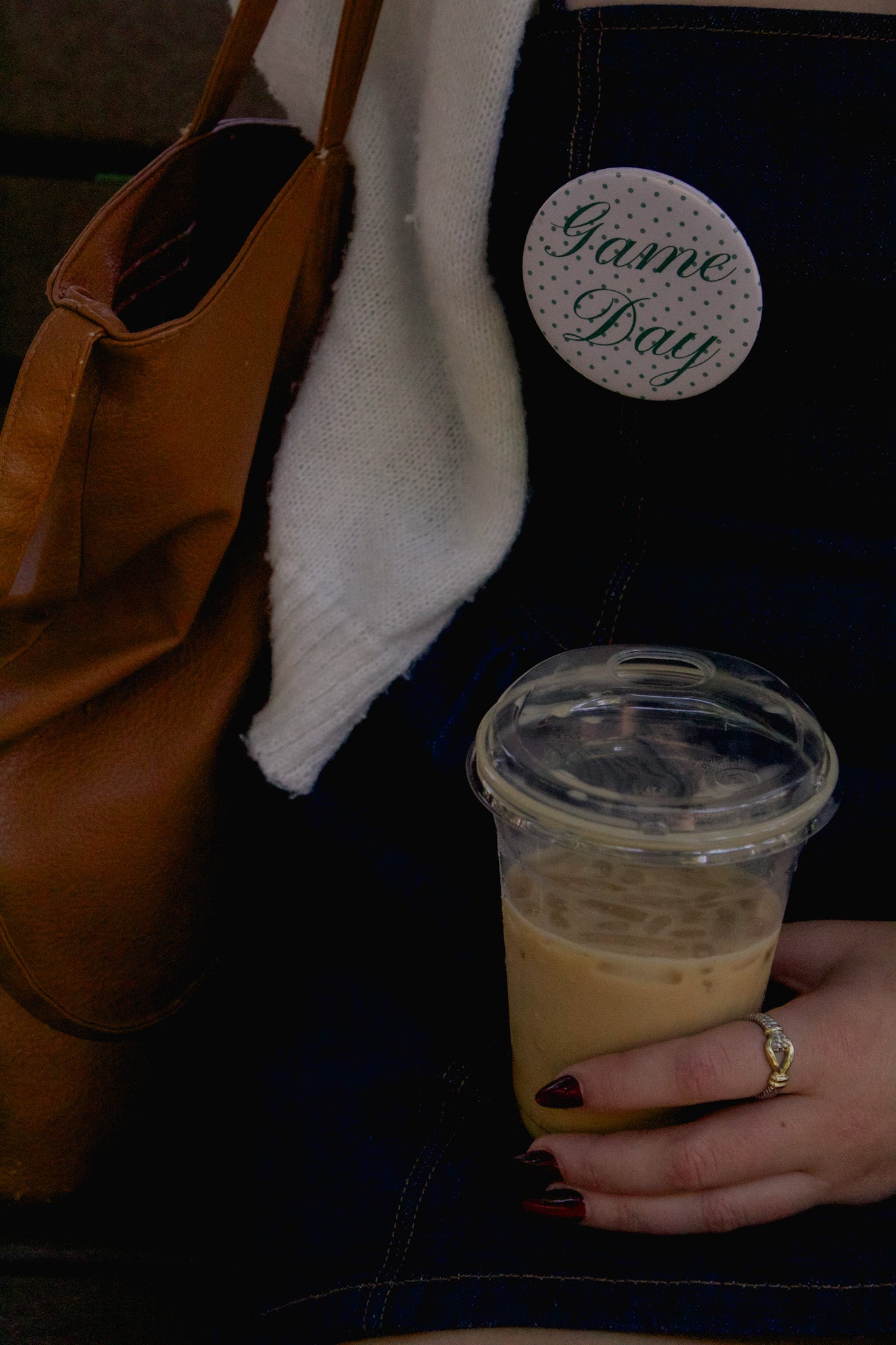 Hand holding a cup of coffee next to a brown bag with 'Game Day' button
